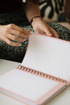 A woman turns pages in a spiral-bound notebook, emphasizing writing and planning.